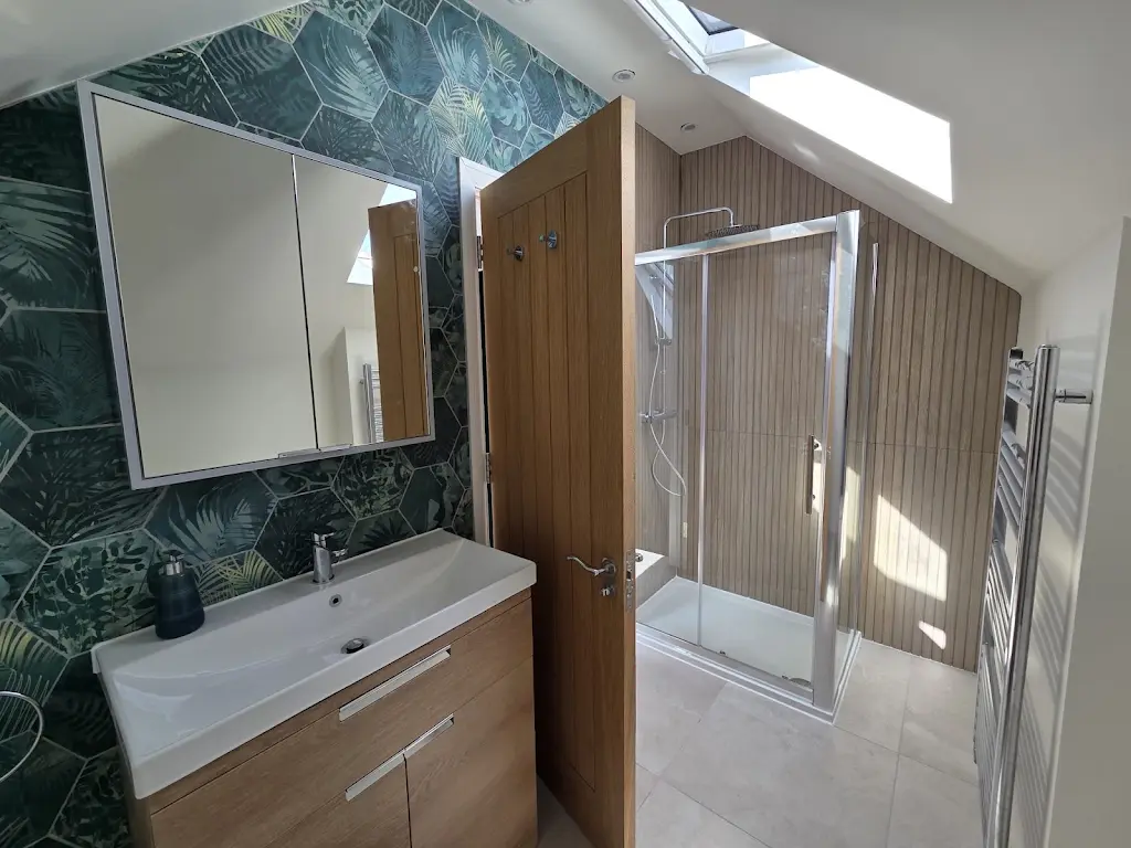 Finished bathroom with a green hexagonal feature wall behind the basin, wood-effect tiling in the shower enclosure and large-format floor tiles.