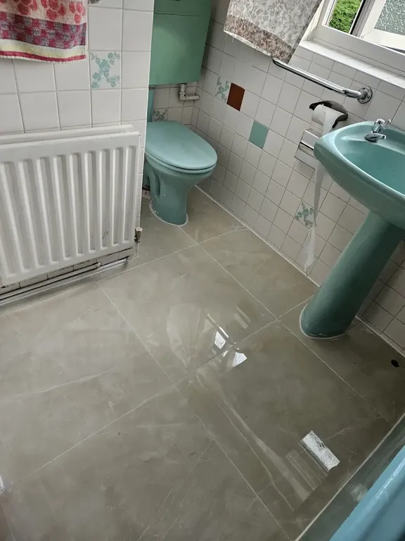 Bathroom finished with large light floor tiles cut neatly around the radiator, basin pedestal and WC.
