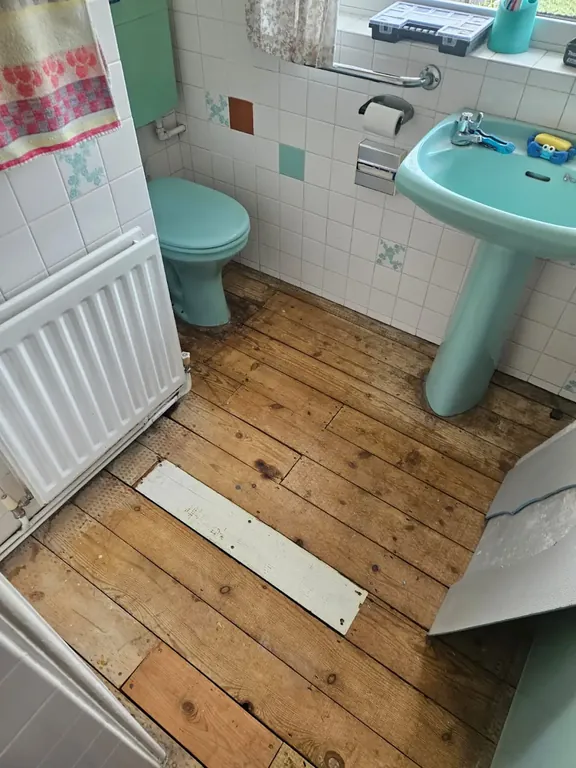 Bathroom with bare timber floorboards lifted and exposed, with the original suite and patterned wall tiles still in place.