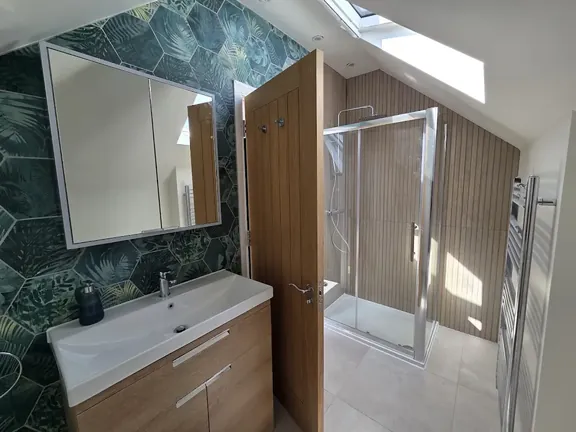 Finished bathroom with a green hexagonal feature wall behind the basin, wood-effect tiling in the shower enclosure and large-format floor tiles.