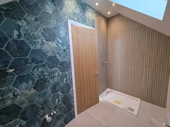 Green hexagonal wall tiles fitted around a doorway, with vertical wood-effect tiles lining the shower area and the tray set in place.