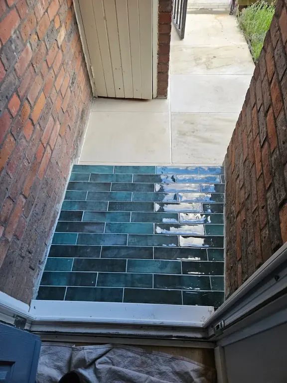 Front doorstep tiled in deep teal rectangular tiles set between the brick piers, with stone paving beyond.