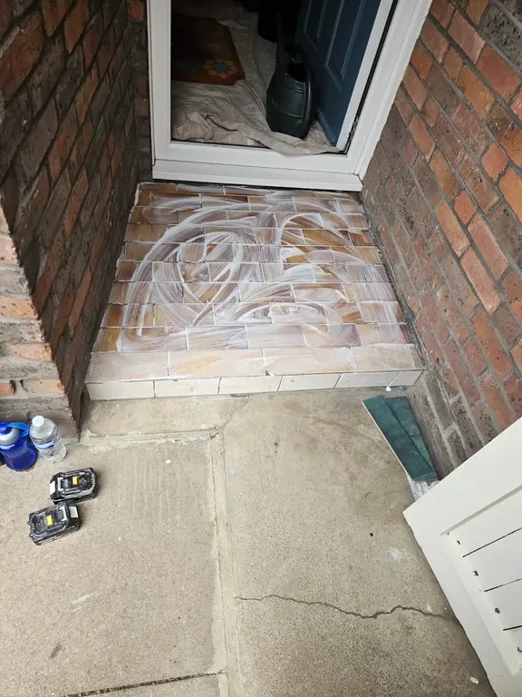 Front doorstep primed and ready between brick piers, with tools and adhesive set out.
