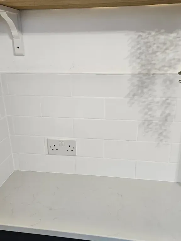 Kitchen alcove tiled in white metro tiles, cut around the socket and finished neatly down to the worktop.