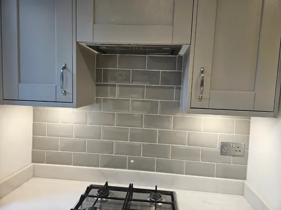 Grey metro tiles laid in a brick bond pattern behind the hob and extractor, running neatly between the wall units.
