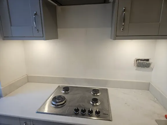 Kitchen wall behind the hob left bare and painted, with no splashback and a socket set into the wall.