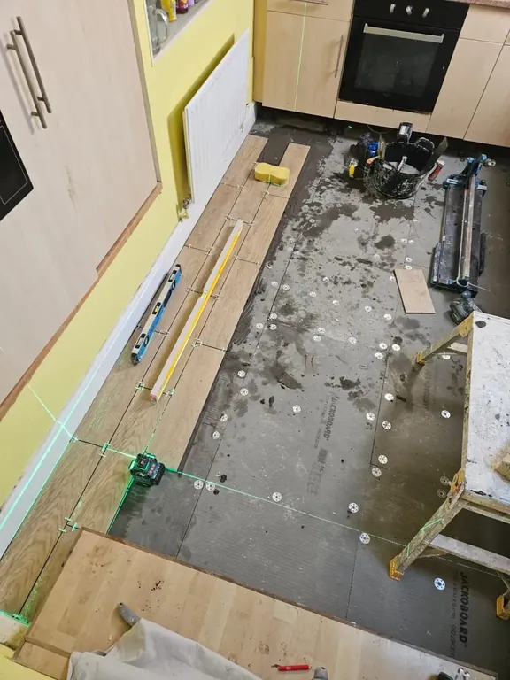 Kitchen subfloor levelled and marked out with a laser line, with the first plank tiles started at the doorway.