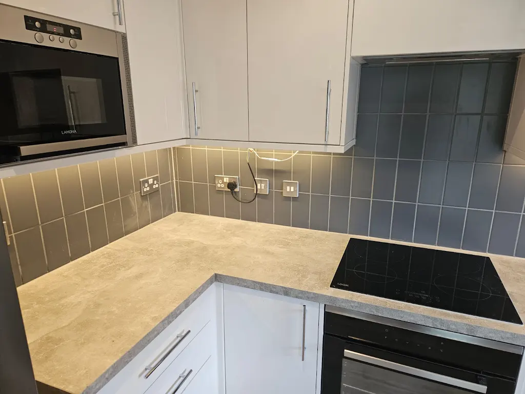 Pale grey metro tiles fitted in a stacked pattern along the worktop run, cut around the sockets and lit by under-cabinet lighting.