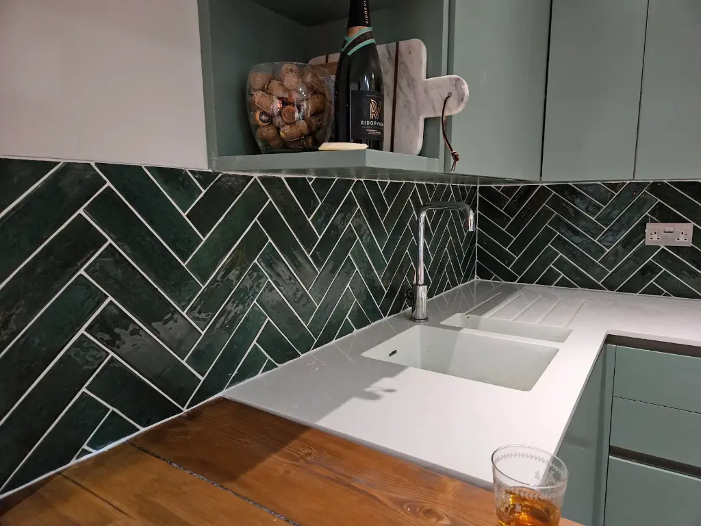 Close view of the dark green herringbone splashback showing the cut and joint lines around the tap and the shelved recess.